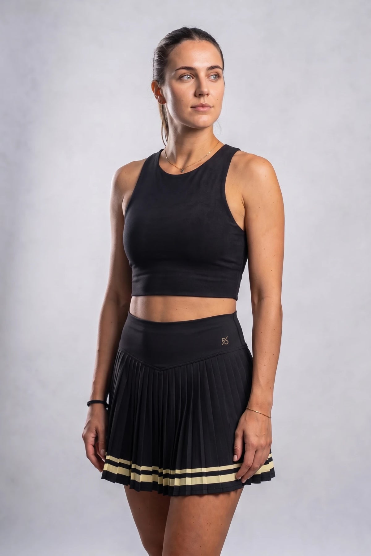 The Aura Court Skirt in Black Onyx, three-quarter studio view showing the V-shaped waistband and pleated skirt #Color_Black Onyx