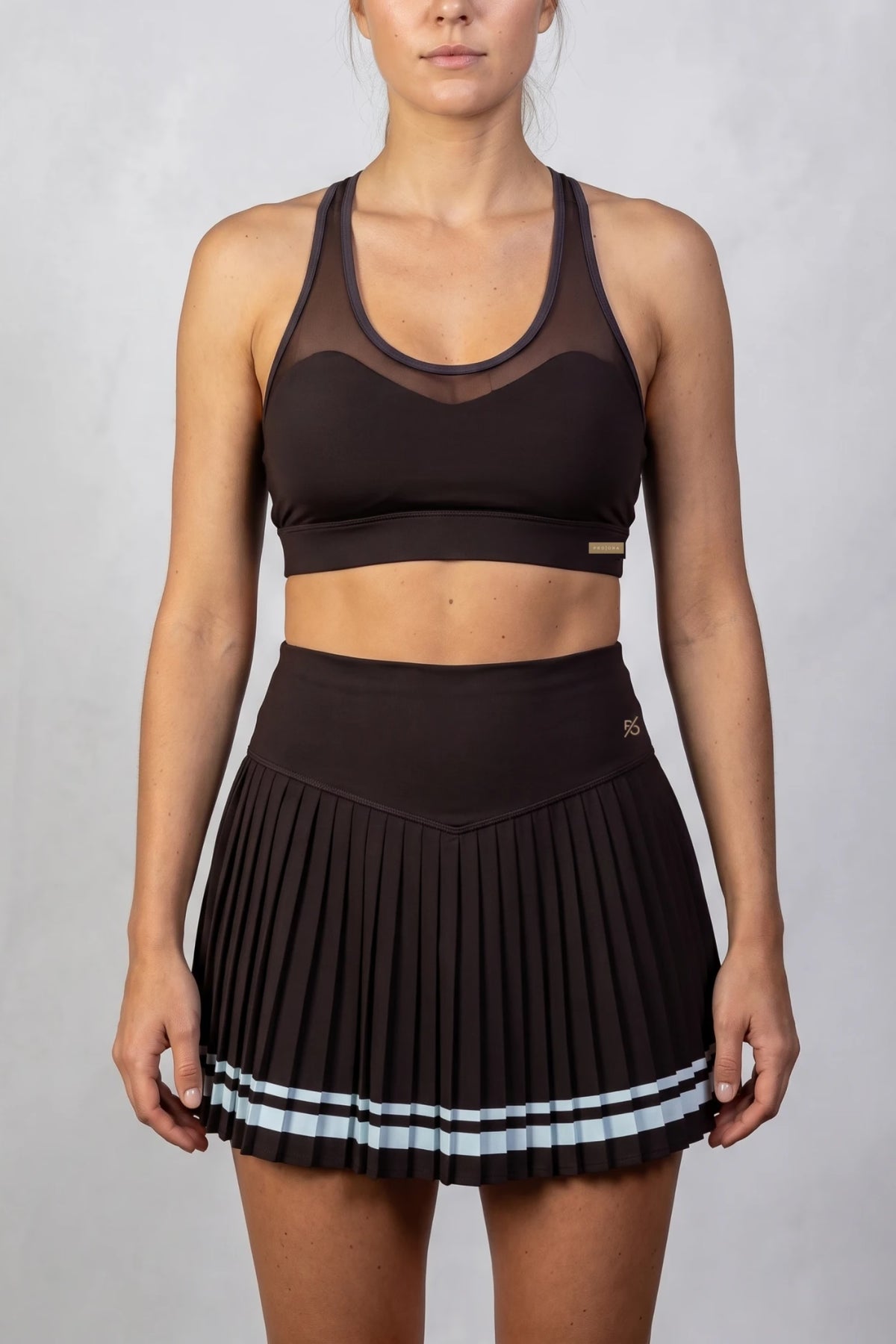 The Aura Court Skirt in Dark Espresso, studio front view showing the V-shaped waistband and pale blue striped hem #Color_Dark Espresso