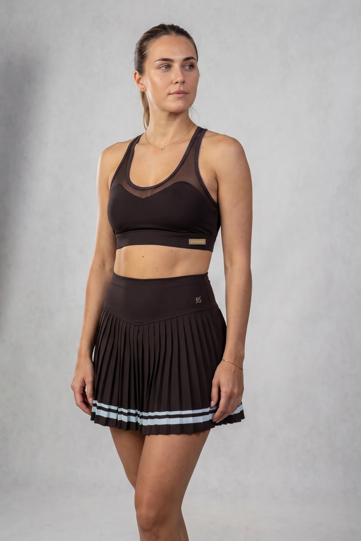 The Aura Court Skirt in Dark Espresso, three-quarter studio view showing the pleated skirt and waistband #Color_Dark Espresso