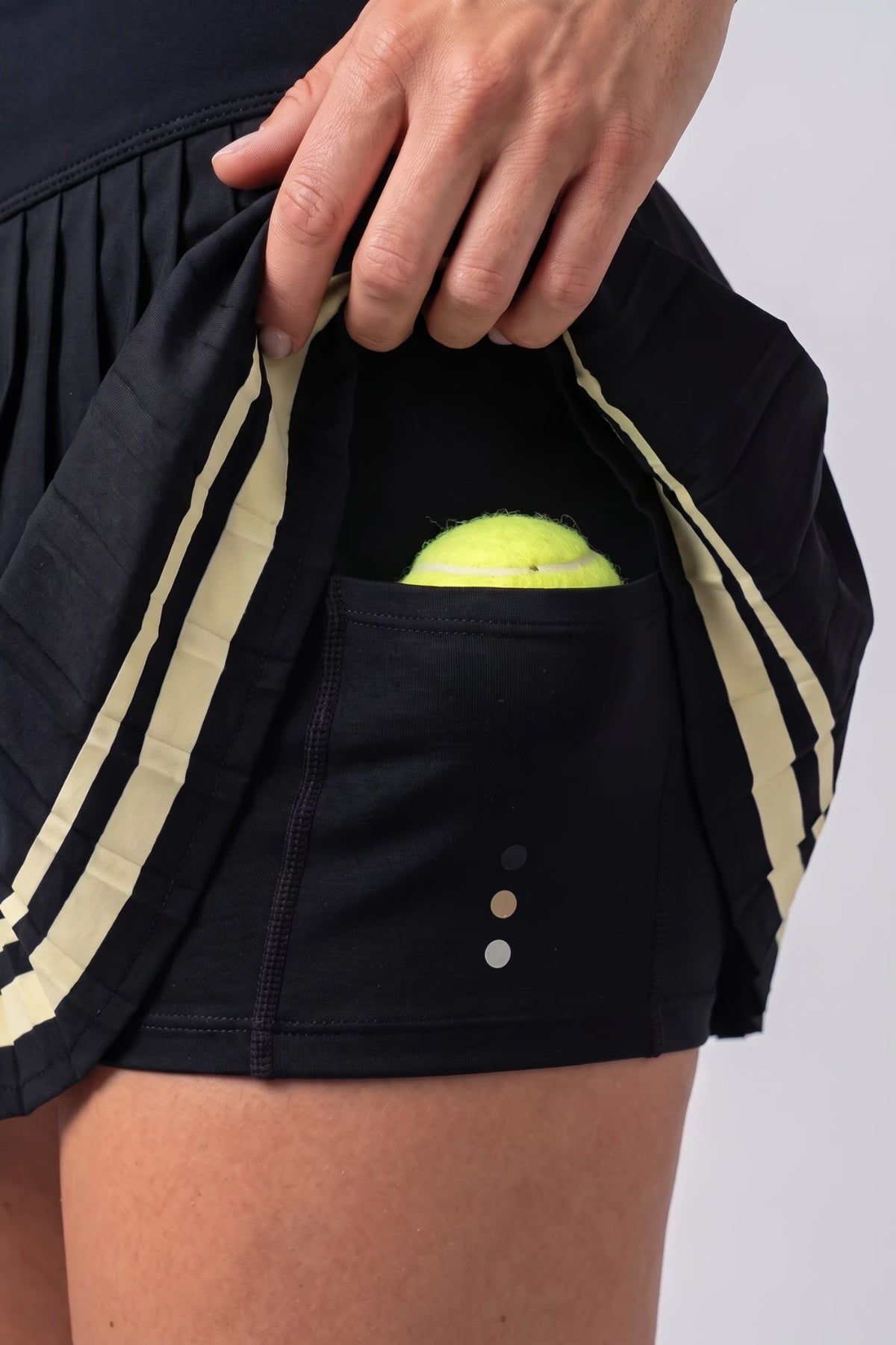 Close-up of the Black Onyx Aura Court Skirt showing the built-in shorts and pocket holding a tennis ball #Color_Black Onyx