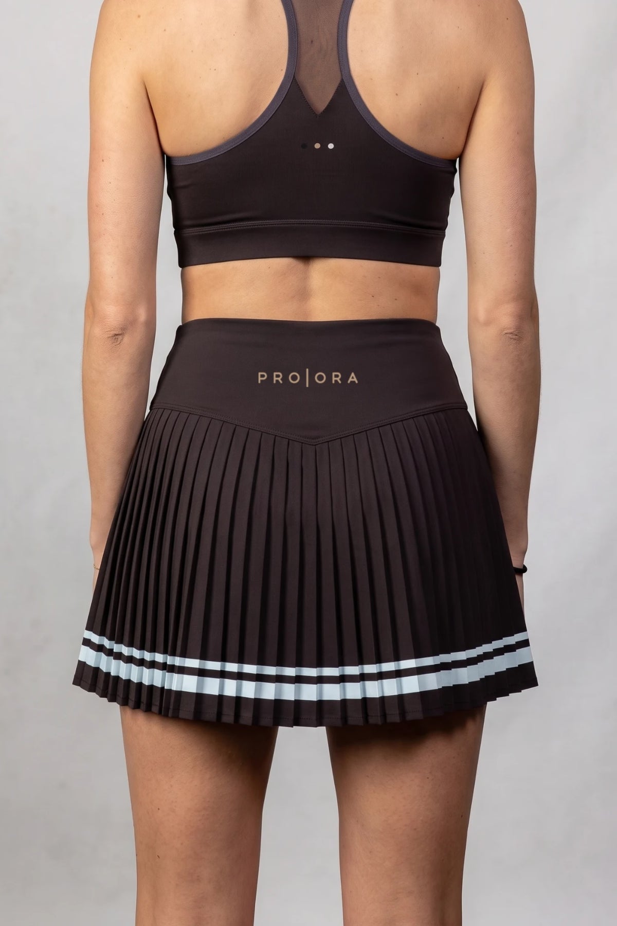 The Aura Court Skirt in Dark Espresso, back view showing the pleats, pale blue striped hem and PRO | ORA waistband logo #Color_Dark Espresso
