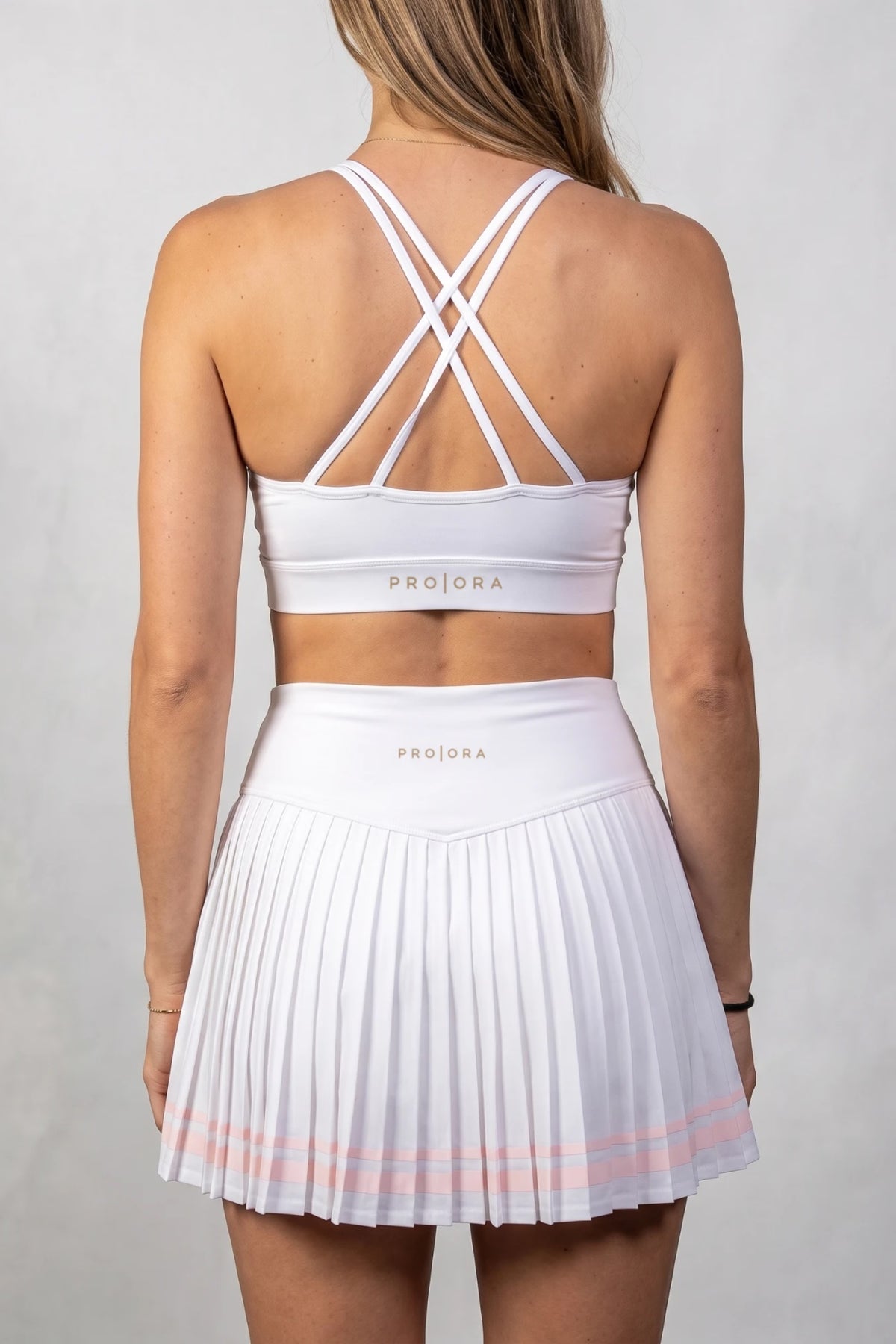 The Aura Court Skirt in White Onyx, back view showing the pleats, pink striped hem and PRO | ORA waistband logo #Color_White Onyx