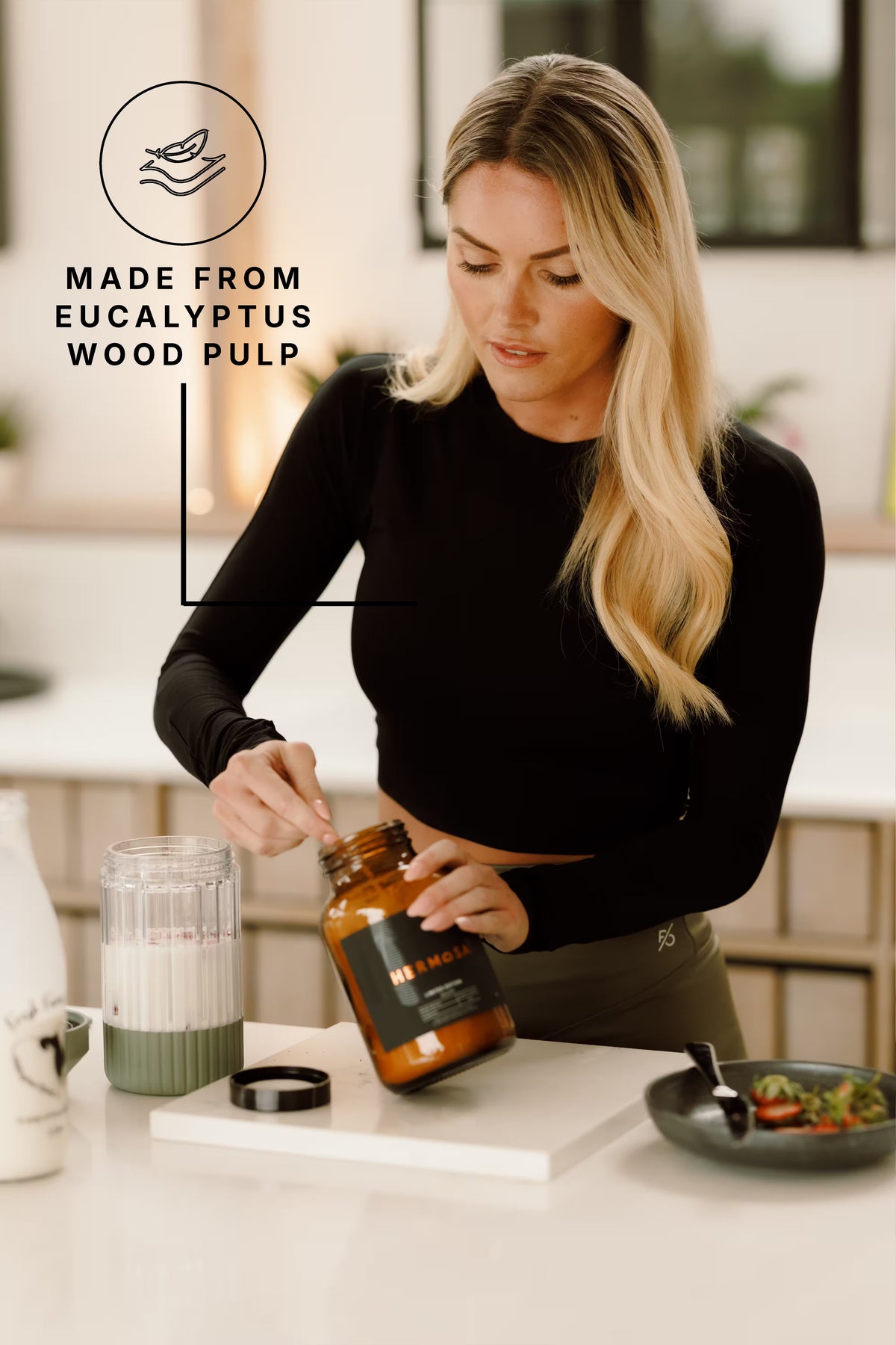 Woman in a black PRO | ORA long sleeve crop top preparing breakfast in a bright kitchen, with a roundel reading Made from eucalyptus wood pulp